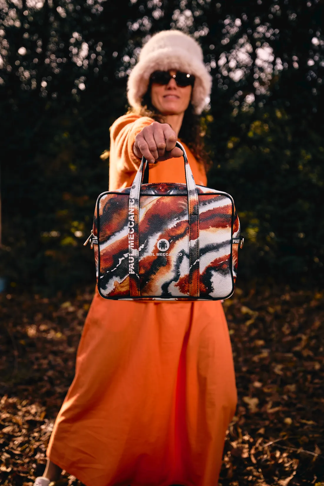 Eine Frau in orangefarbenem Kleid und Pelzmütze mit einer bunten Paul-Meccanico-Tasche